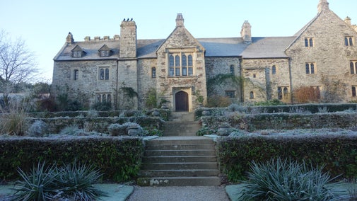 Cotehele's house, an old grey stone building, above steps of a terraced garden covered in frost.